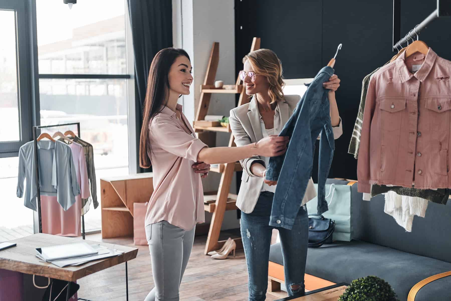 Happy women selecting clothing in trendy boutique store in a retail upsystem.